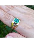 A 18k yellow gold ring with a bezel set genuine colombian emerald on a hand against a natural background.
