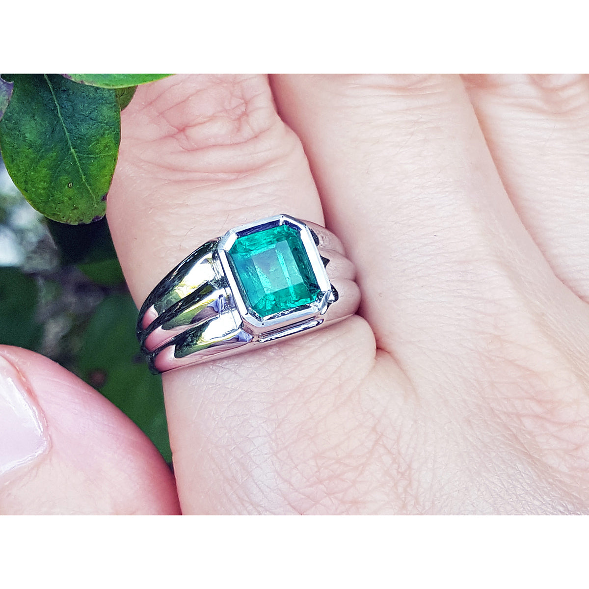 White gold ring for man with a square natural emerald on a finger against a natural background.