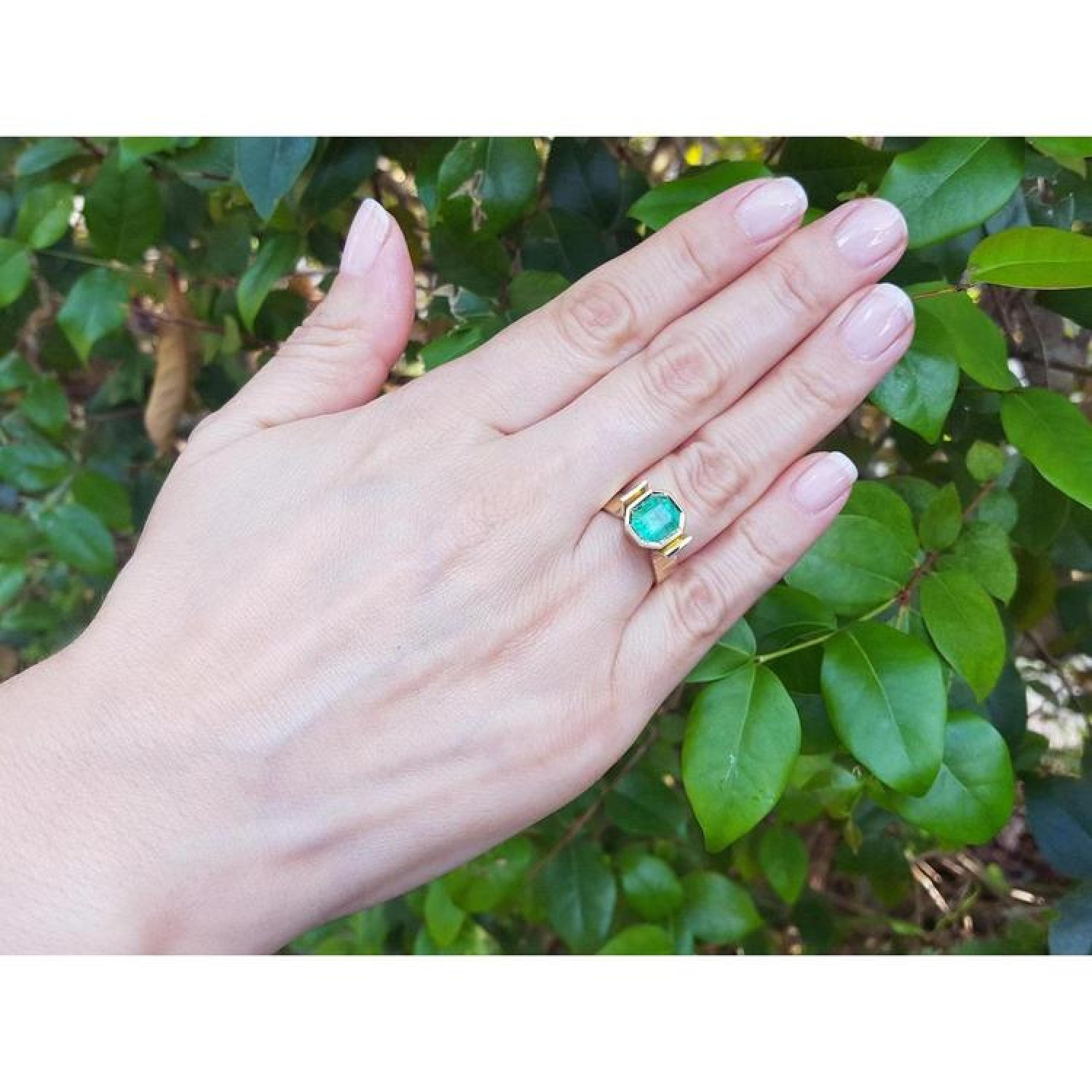 2.14 ct rectangular Colombian emerald solitaire ring, bezel set in 14K yellow gold on a hand.