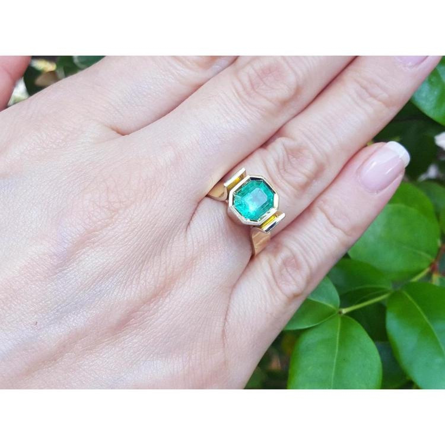 2.14 ct. rectangular Colombian emerald solitaire ring, bezel set in 14K yellow gold on a hand.