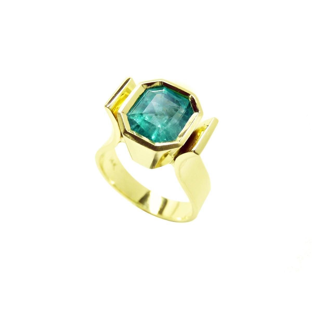 This emerald solitaire ring is on a tilted position, displaying the top bezel and side profile.
