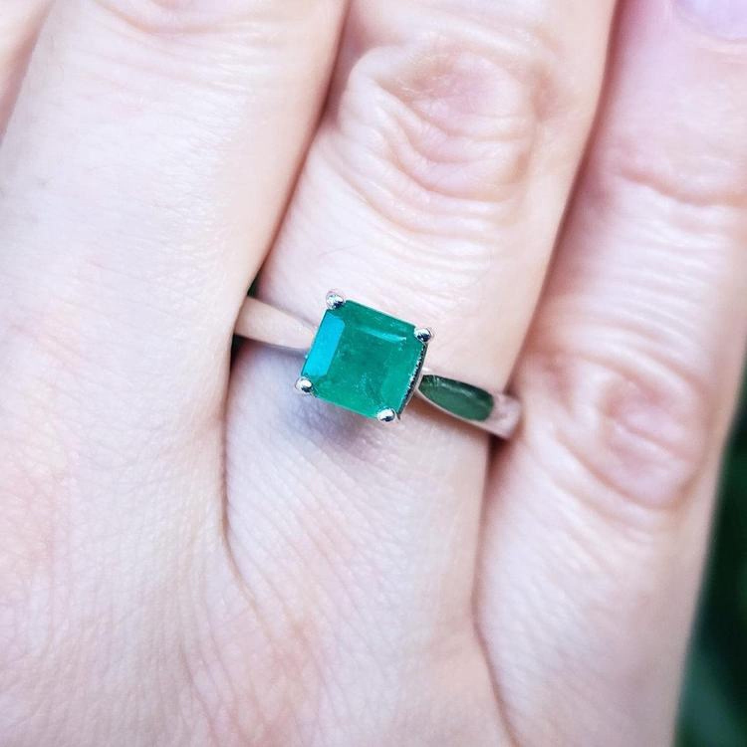 1.00 ct. square emerald cut Colombian emerald solitaire silver ring on a finger.