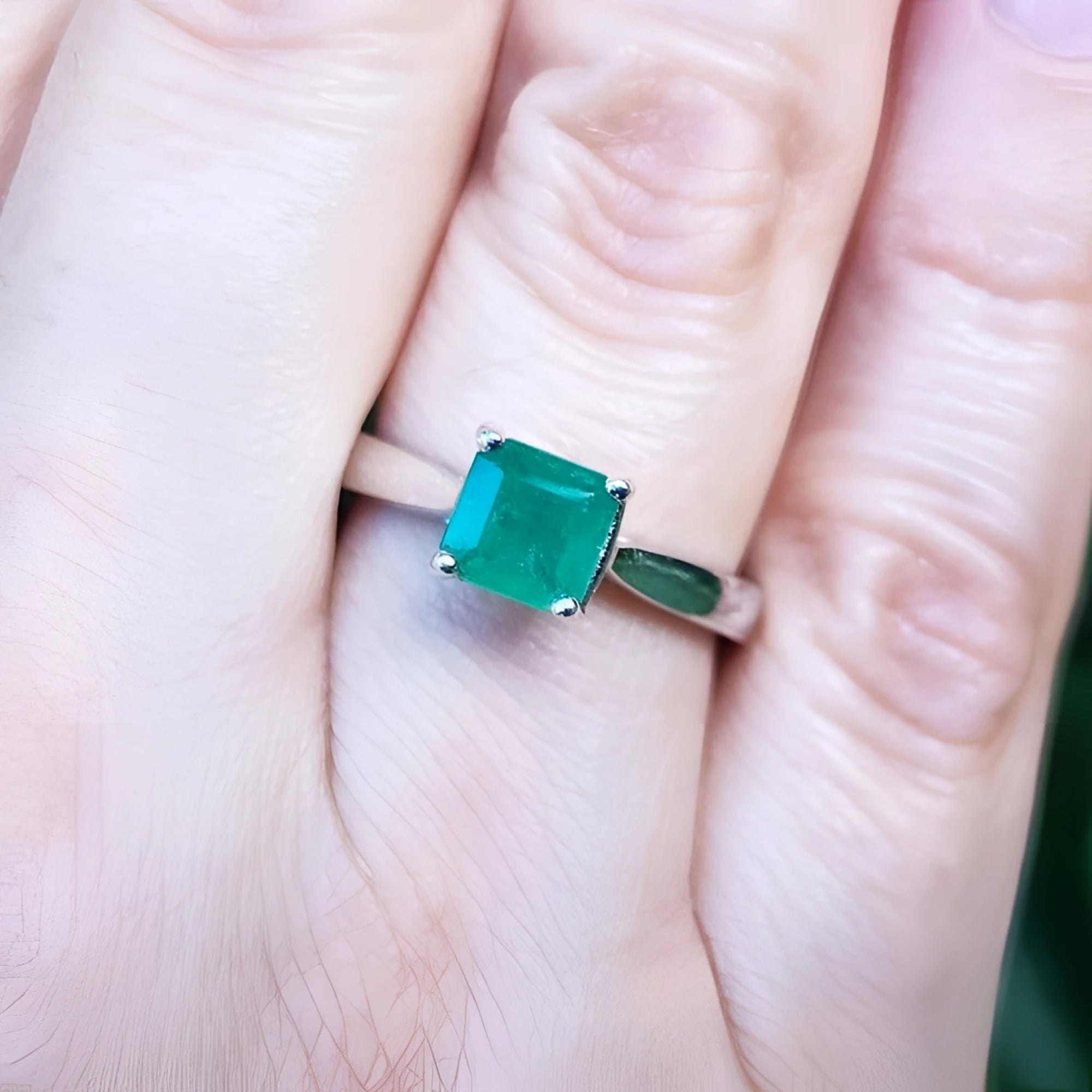 1.00 ct. square emerald cut Colombian emerald solitaire silver ring on a finger.