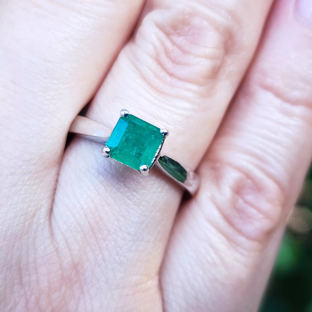 A genuine colombian emerald solitaire silver ring on a finger with a blurred background