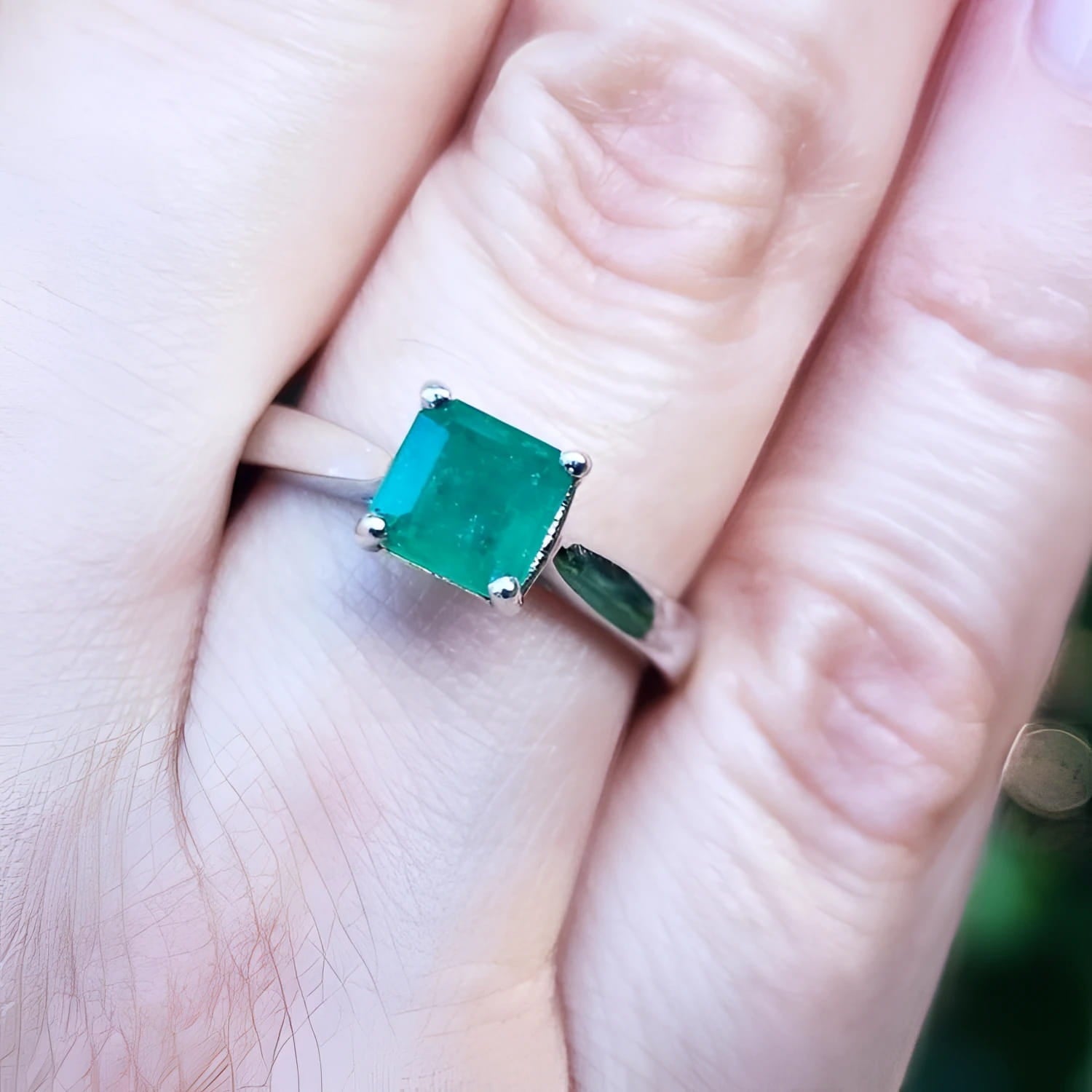 A genuine colombian emerald solitaire silver ring on a finger with a blurred background
