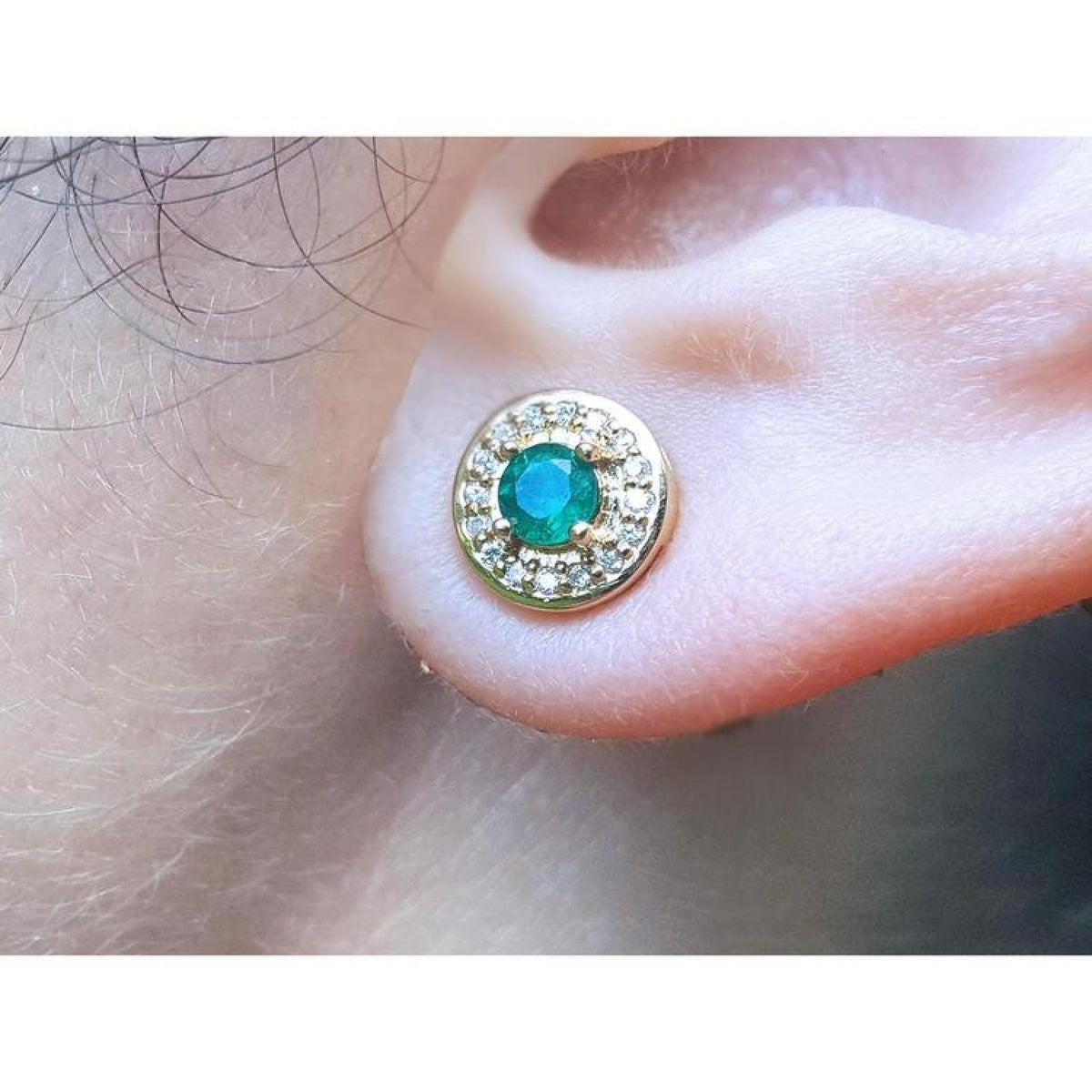 Close-up of a 14k yellow gold emerald stud earring on an ear.