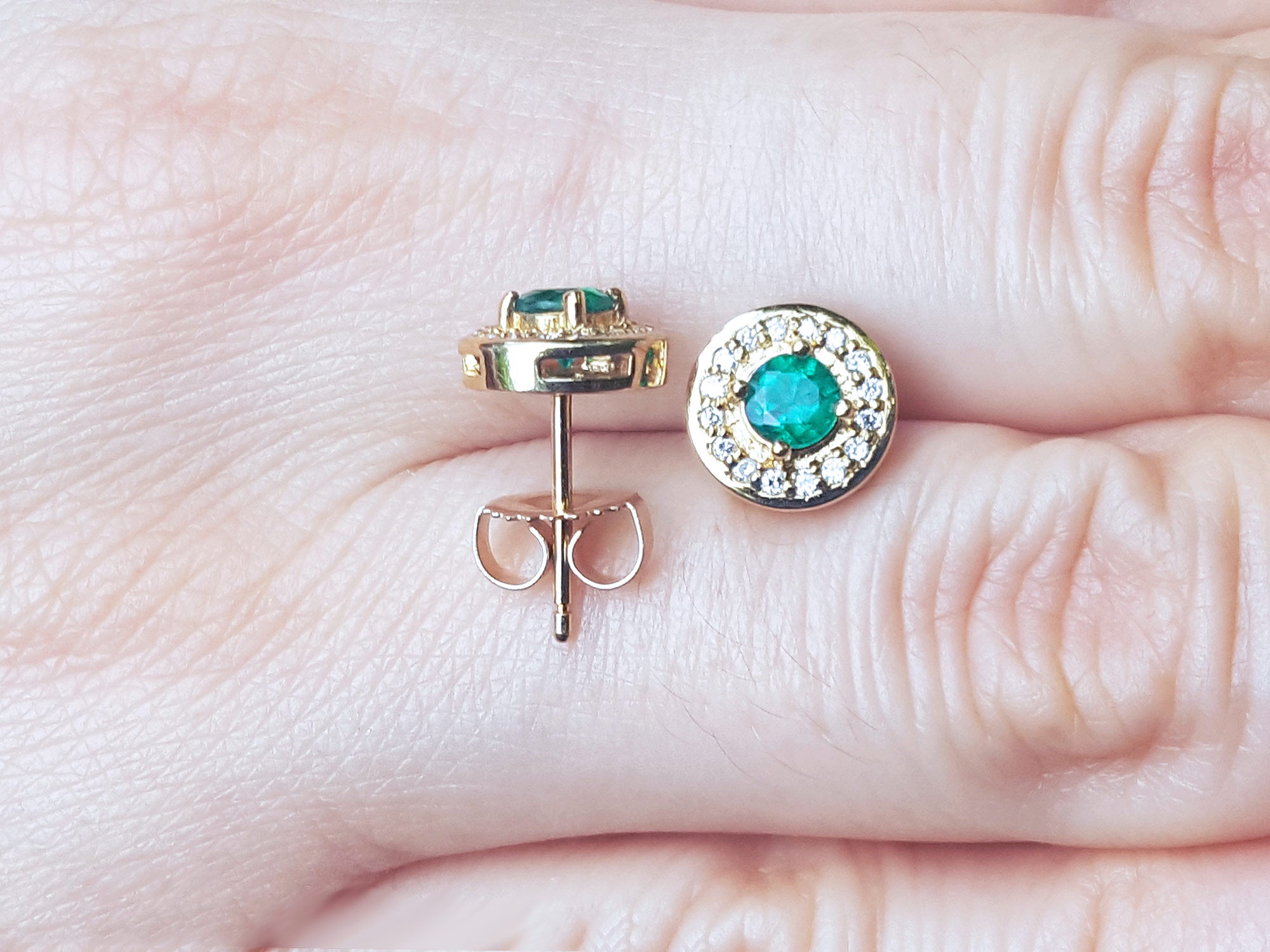 Gold earrings with emerald stones on a hand.