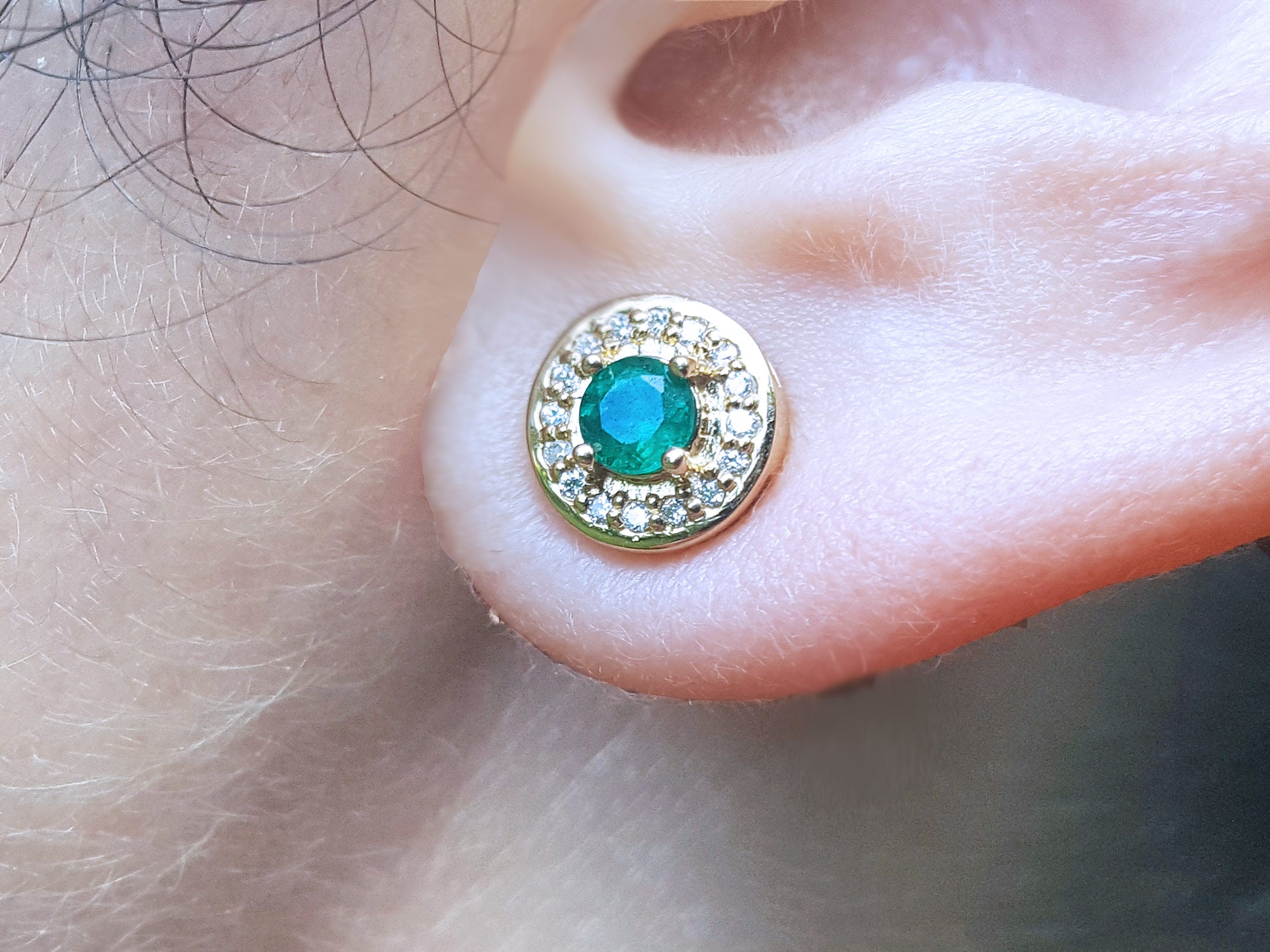 Close-up of a 14k yellow gold emerald stud earring on an ear.
