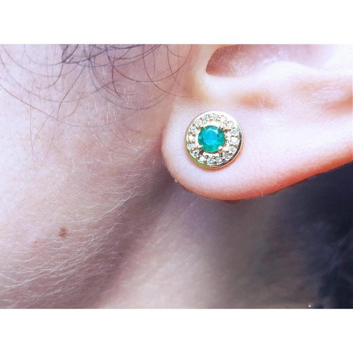 14k yellow gold emerald halo diamond stud earring on an ear.