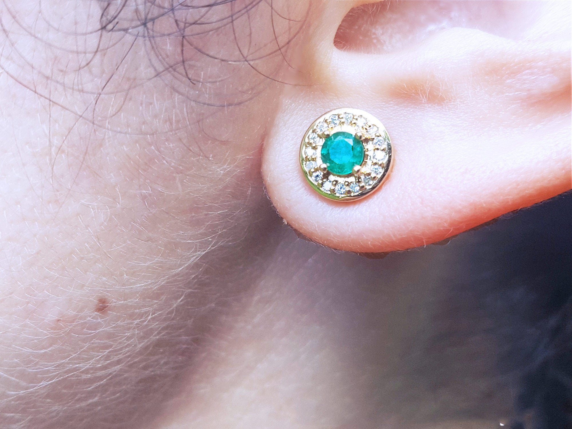Close-up of a 14k gold emerald stud earring on a person&#39;s ear.