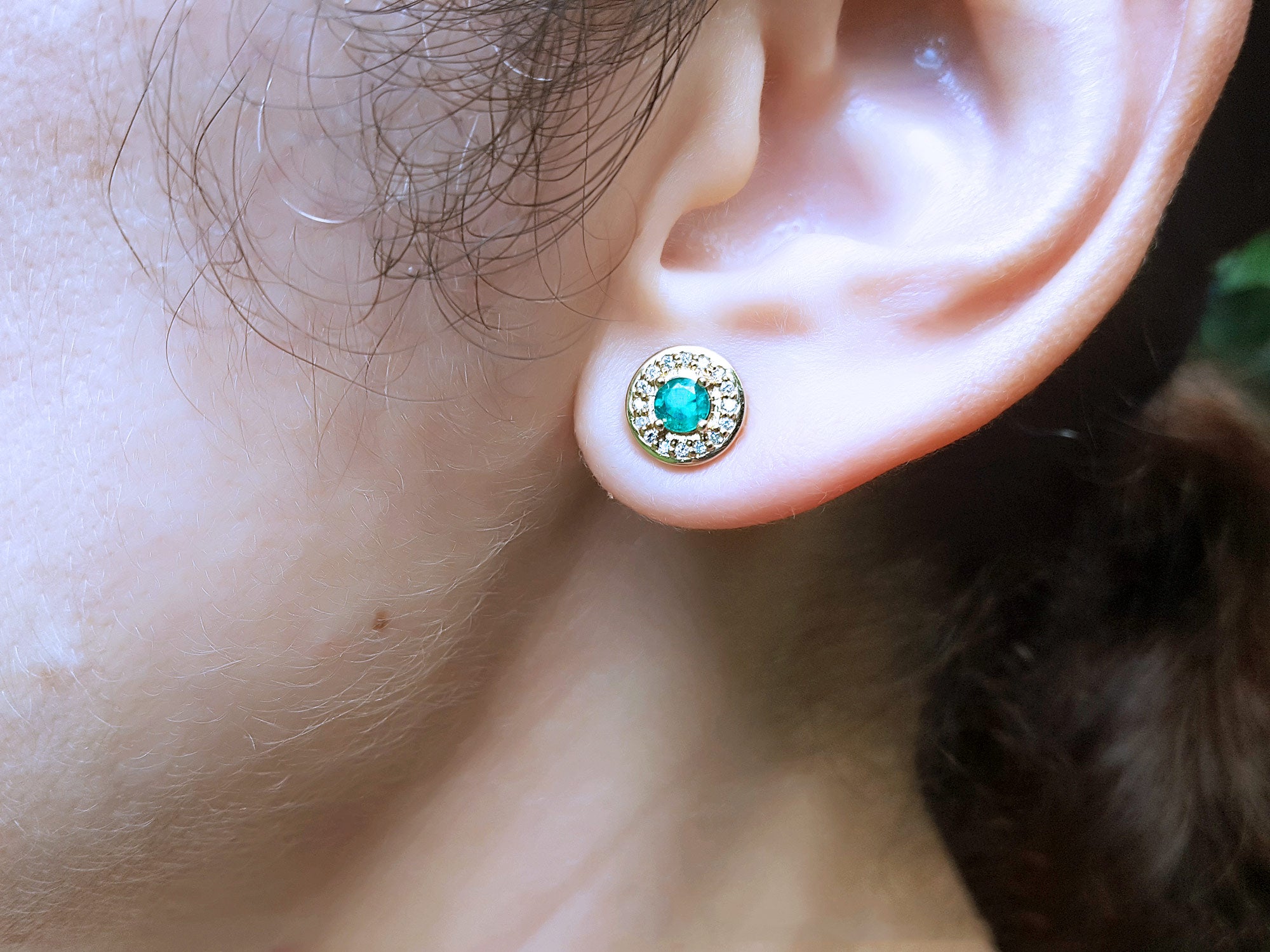 Close-up of a woman&#39;s ear wearing a gold stud emerald earring.