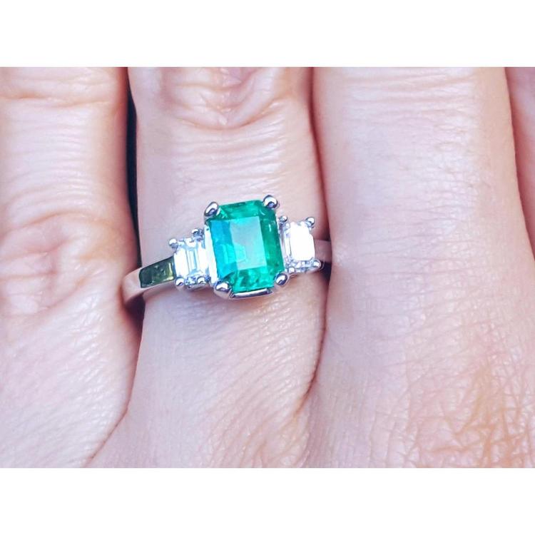Women's emerald three stone ring side genuine emerald cut diamonds crafted in 18k white gold on a finger.