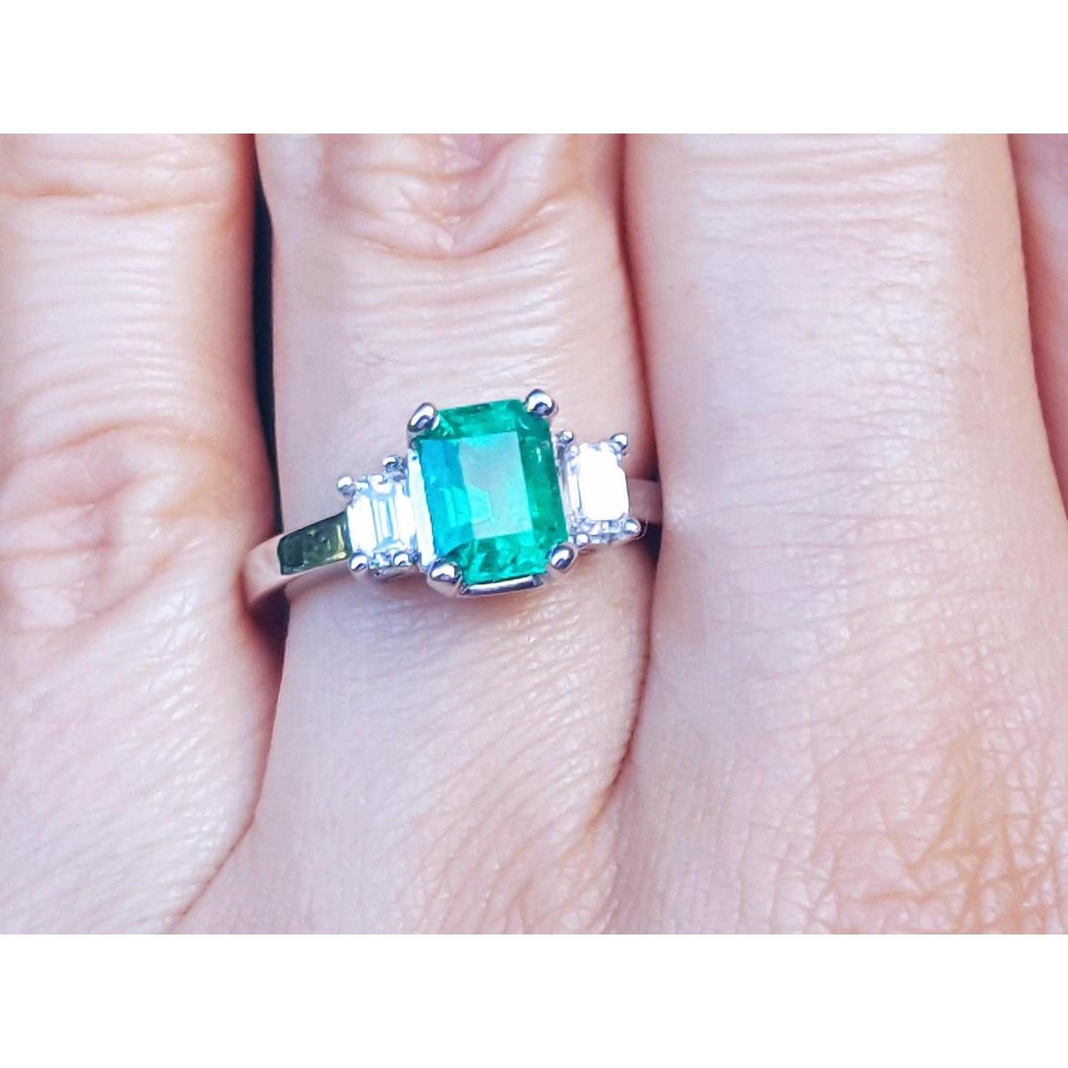 Women's emerald three stone ring side diamonds on a finger