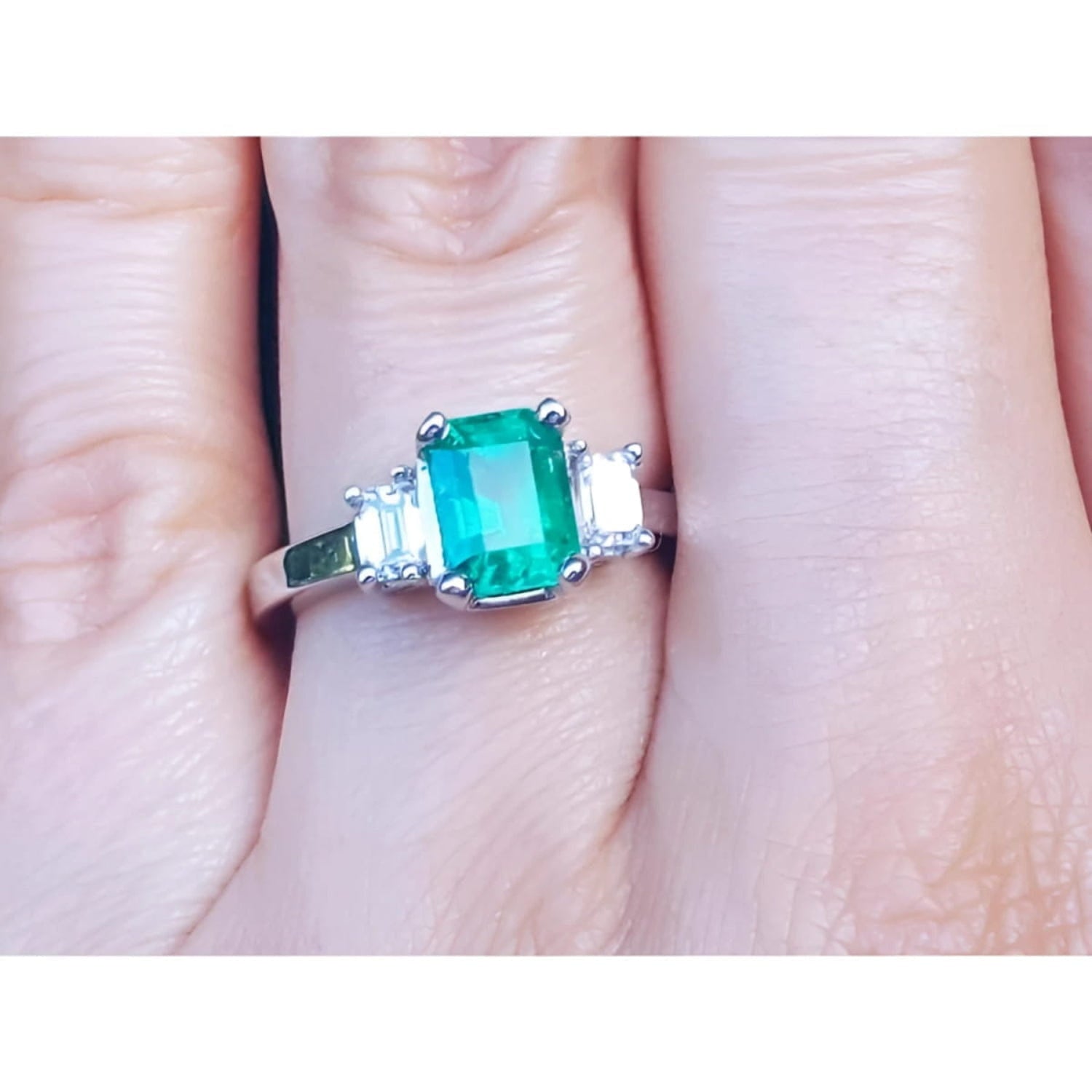 Women's emerald three stone ring side genuine emerald cut diamonds crafted in 18k white gold on a finger.