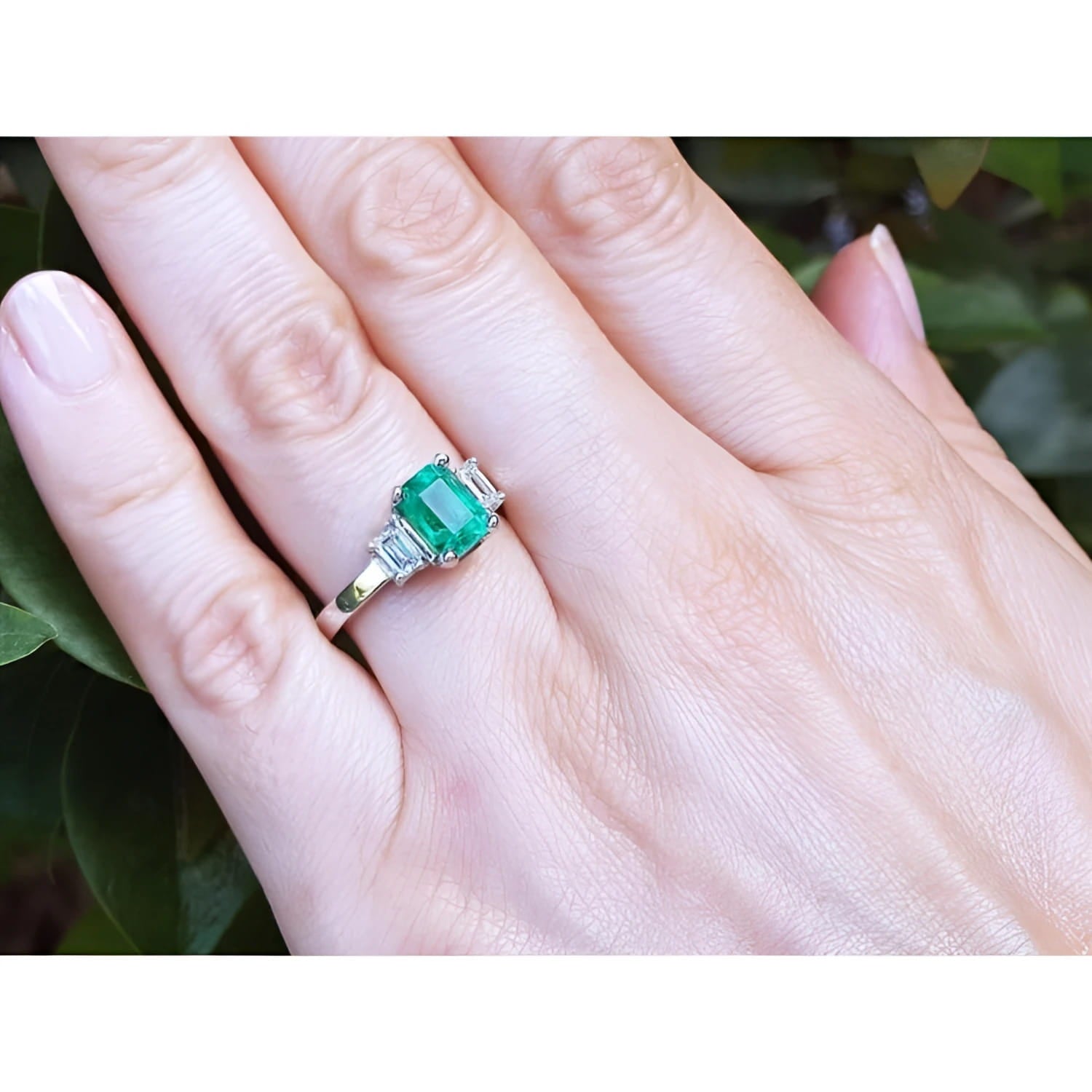 Three stone emerald ring with side diamonds on a hand, crafted in 18K white gold.