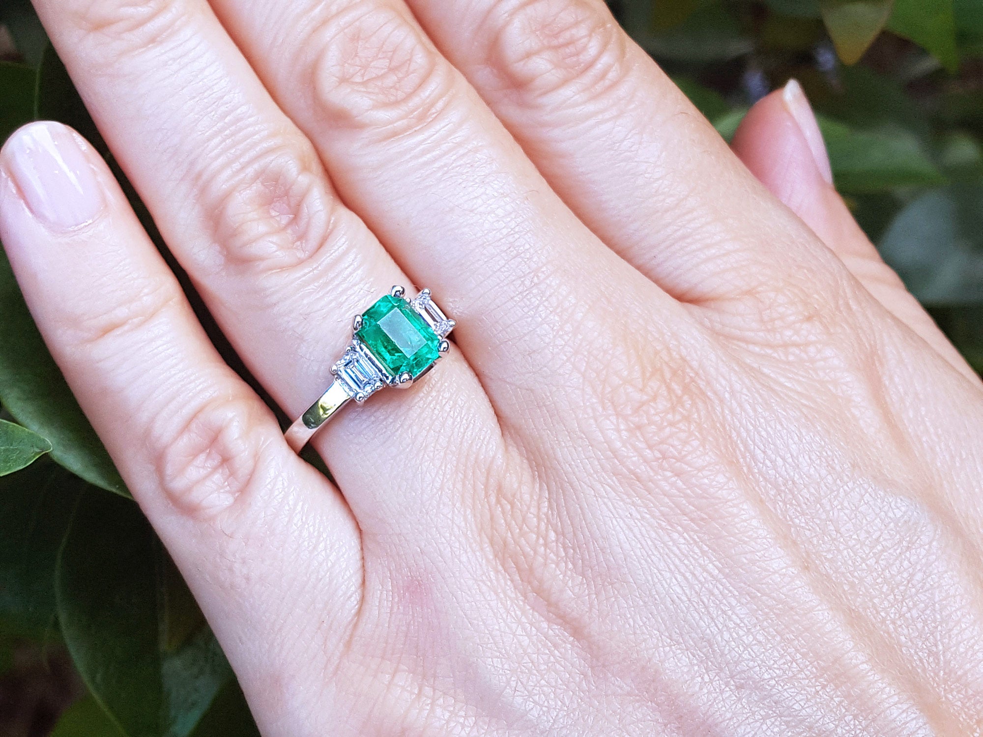 Emerald ring on a hand with a green leafy background