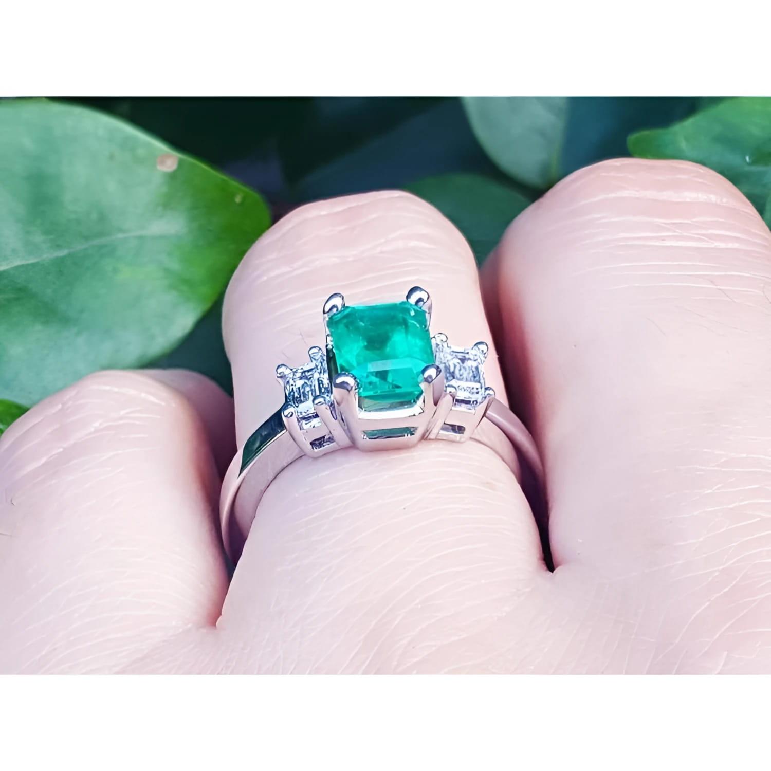 18K white gold three-stone emerald ring with a sparkling bluish-green center stone and side accent diamonds.