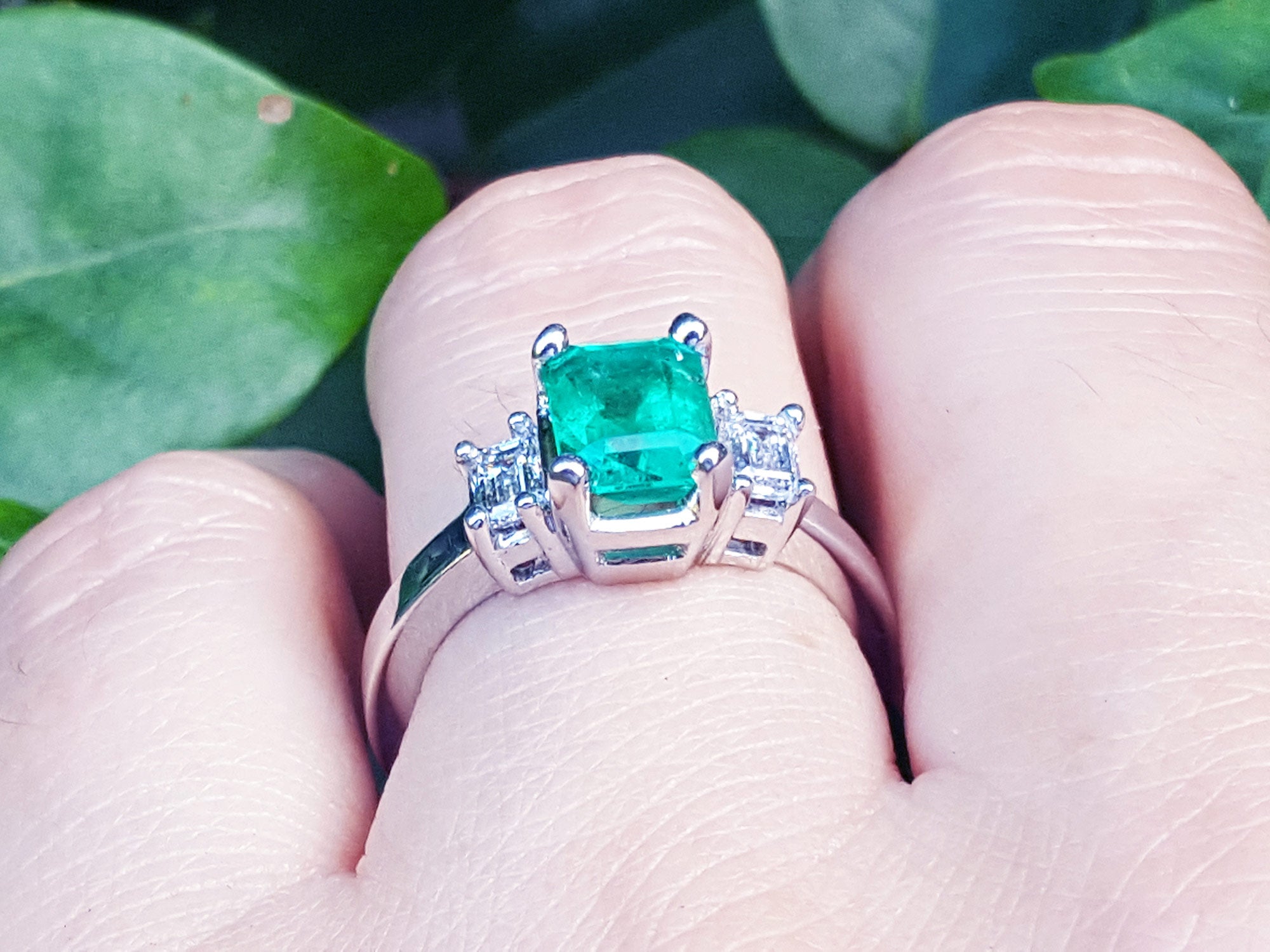 Brides&#39; engagement emerald ring held between fingers against a natural background.