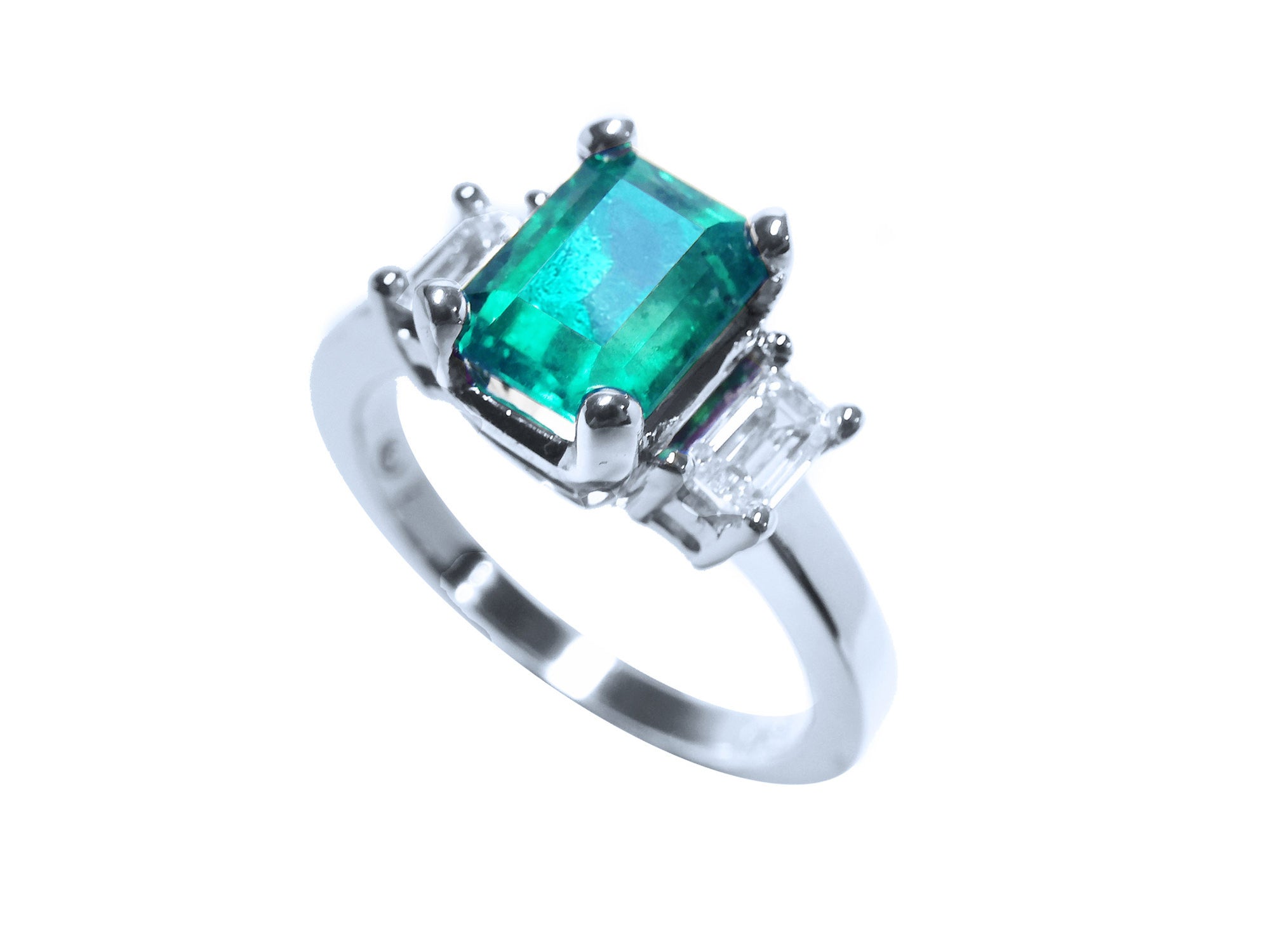 A tilted natural emerald and diamond three stone ring, top and side profile visibles.