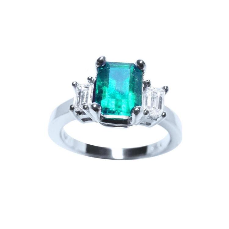 This three stone emerald engagement ring with side natural emerald cut diamonds, is crafted in 18k white gold.