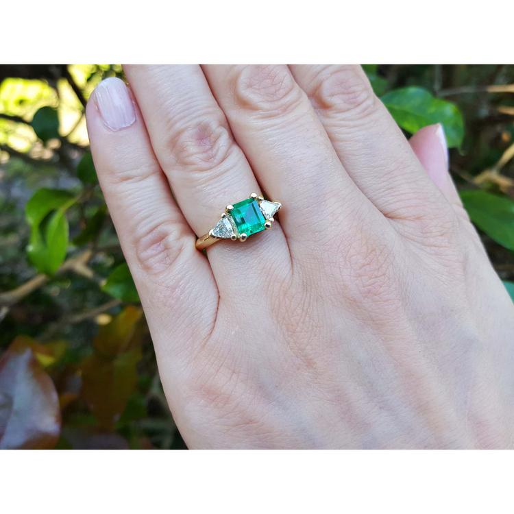 1.48 ct. emerald and trillion side diamond ring in 18K gold on a hand.
