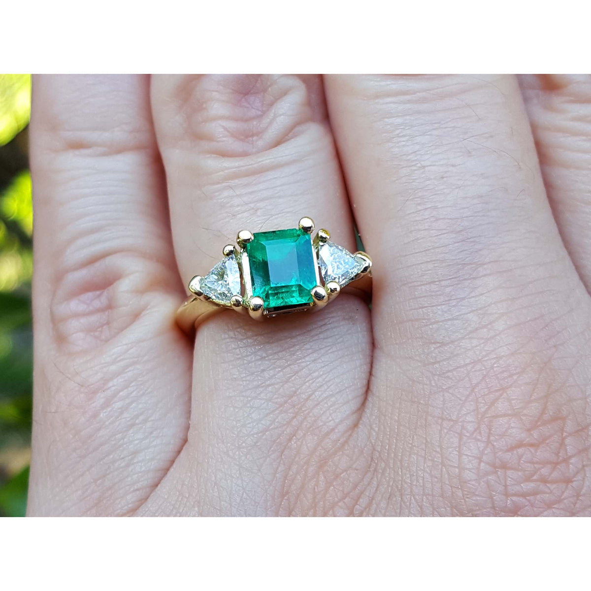 A colombian emerald and trillion side diamond ring in yellow gold on a hand 