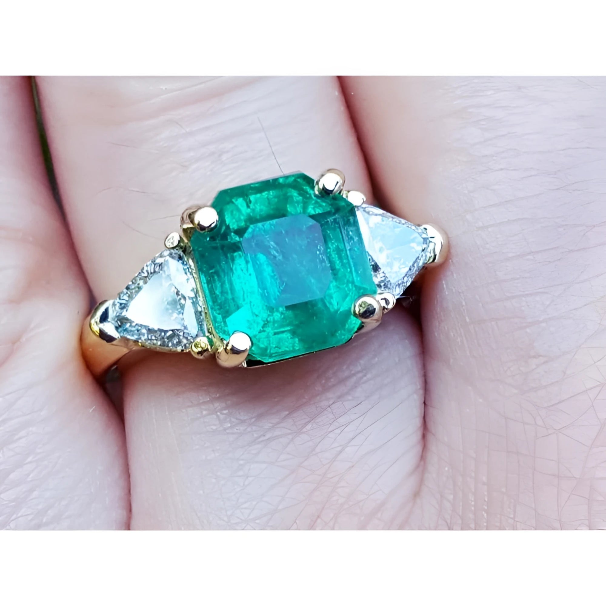 GIA Natural colombian emerald ring with trillion side diamonds in 18k yellow gold setting on a finger.