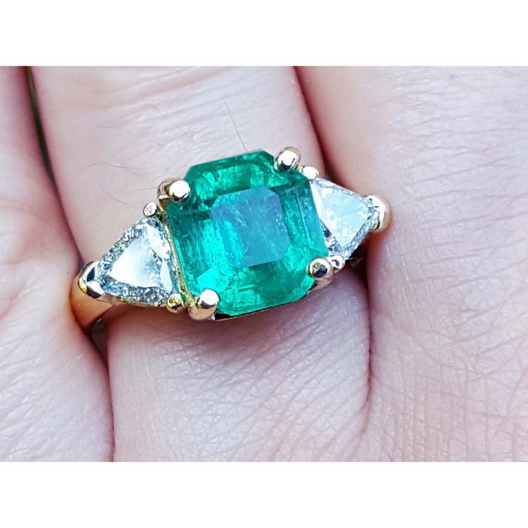 GIA Natural colombian emerald ring with trillion side diamonds in 18k yellow gold setting on a finger.
