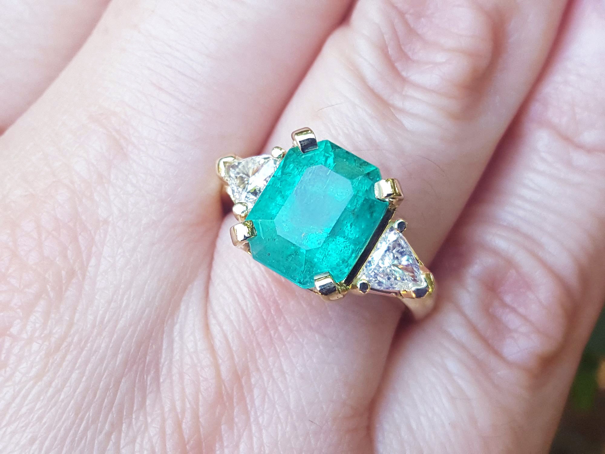 Women's emerald and trillion cut diamond ring on a hand.