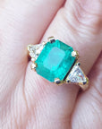 Women's emerald and trillion cut diamond ring on a hand.