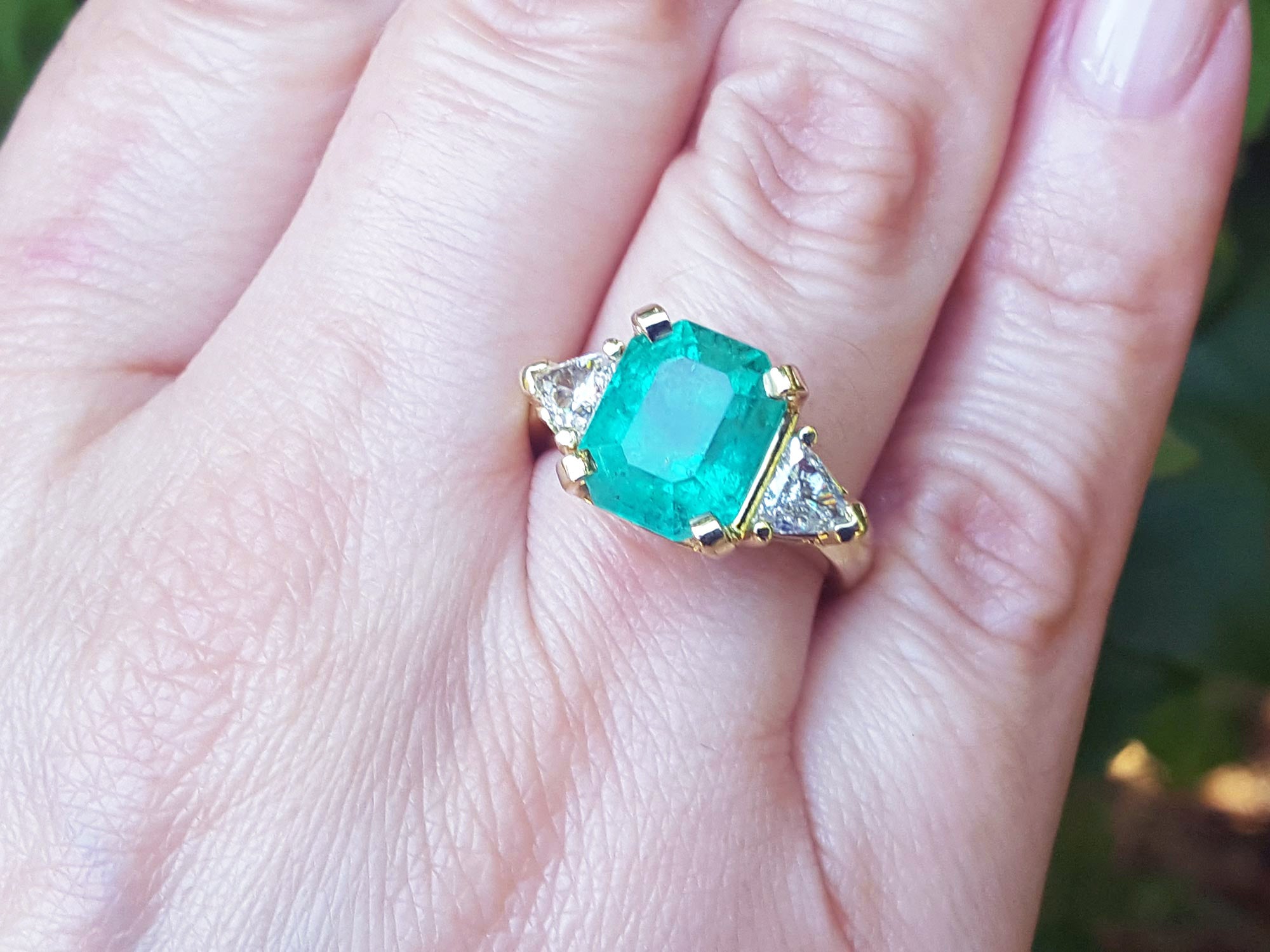 Gold ring with an emerald gemstone on a hand.