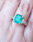 Gold ring with an emerald gemstone on a hand.