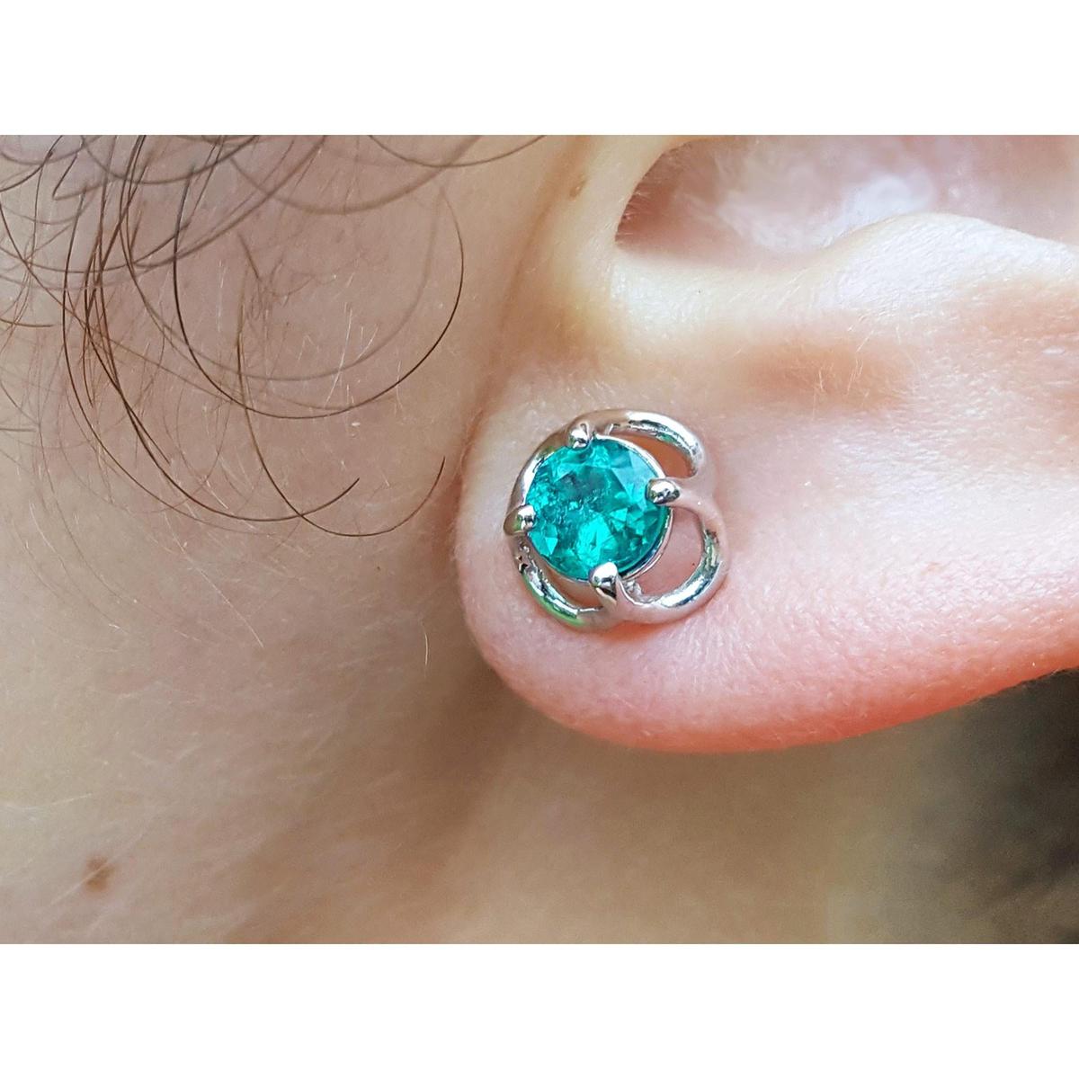 Close-up of a tulip emerald stud earring on an ear.