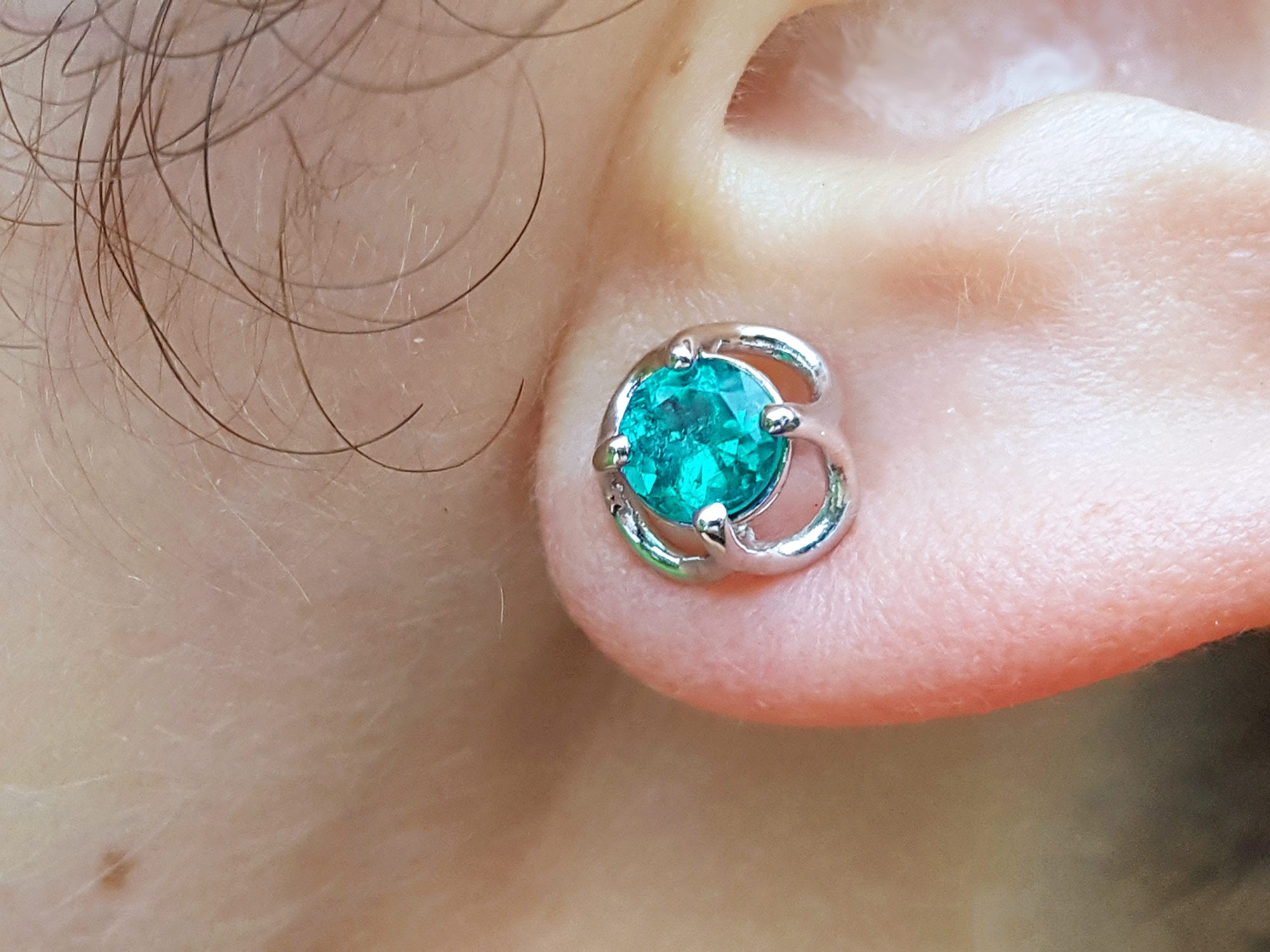 Close-up of a tulip emerald stud earring on an ear.