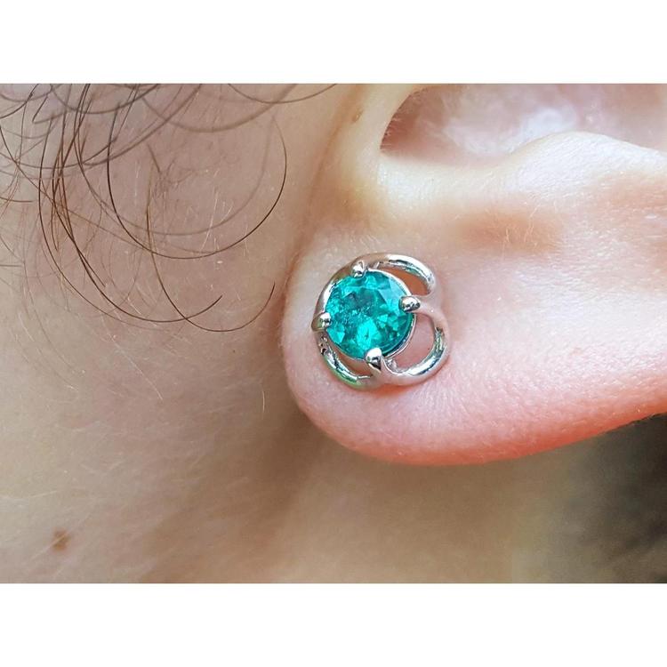Close-up of a tulip emerald stud earring on an ear.