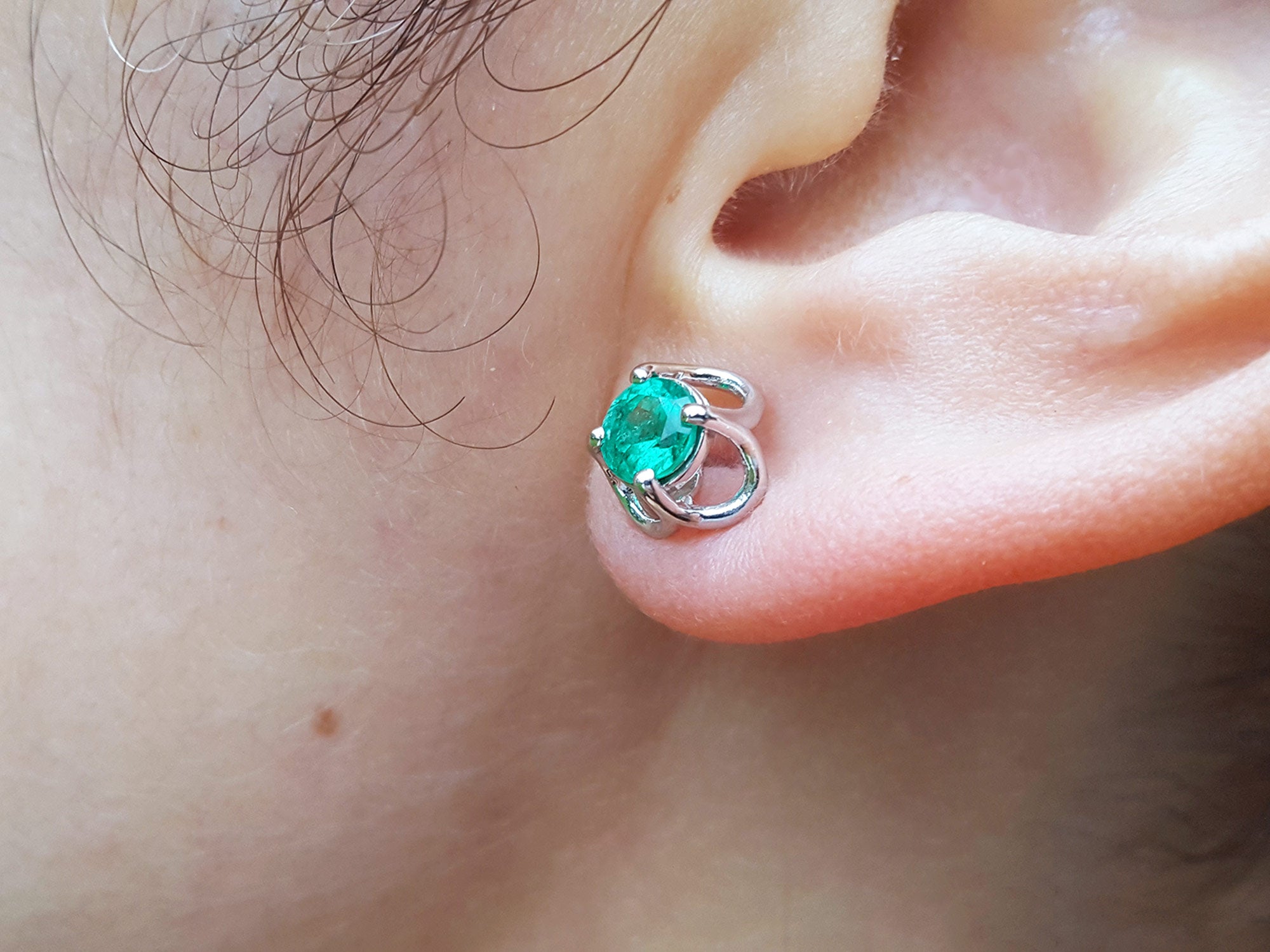 Close-up of an ear wearing a 14k white gold emerald tulip stud earring underside view.