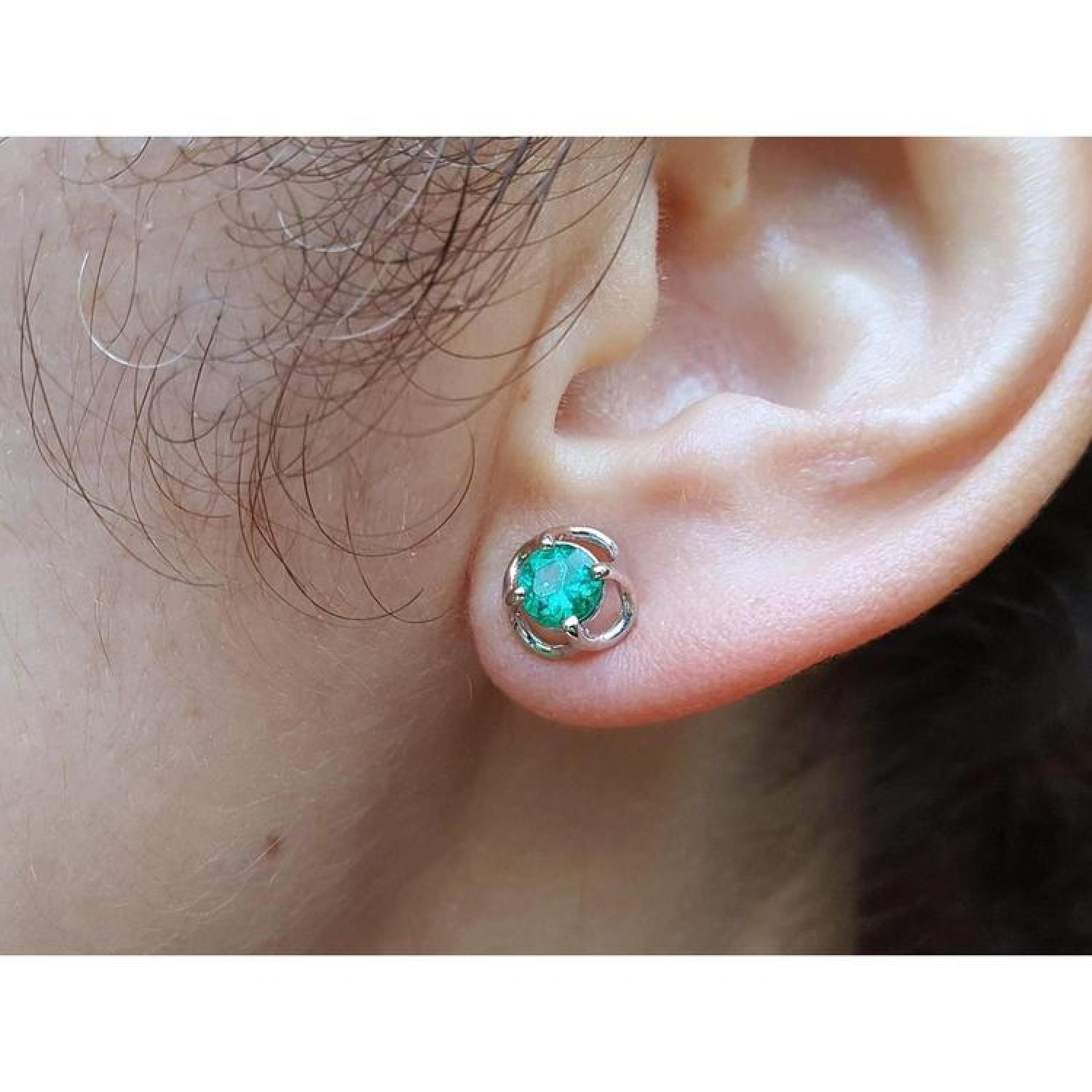 Tulip emerald stud earrings with round green emeralds in 14K white gold, worn on an ear.