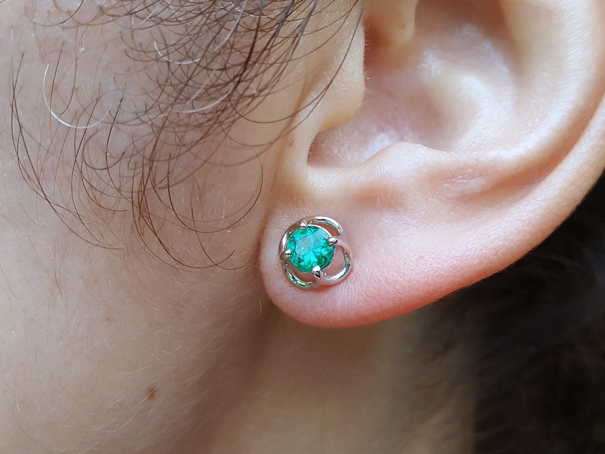Close-up of an ear wearing a Colombian emerald stud earring.