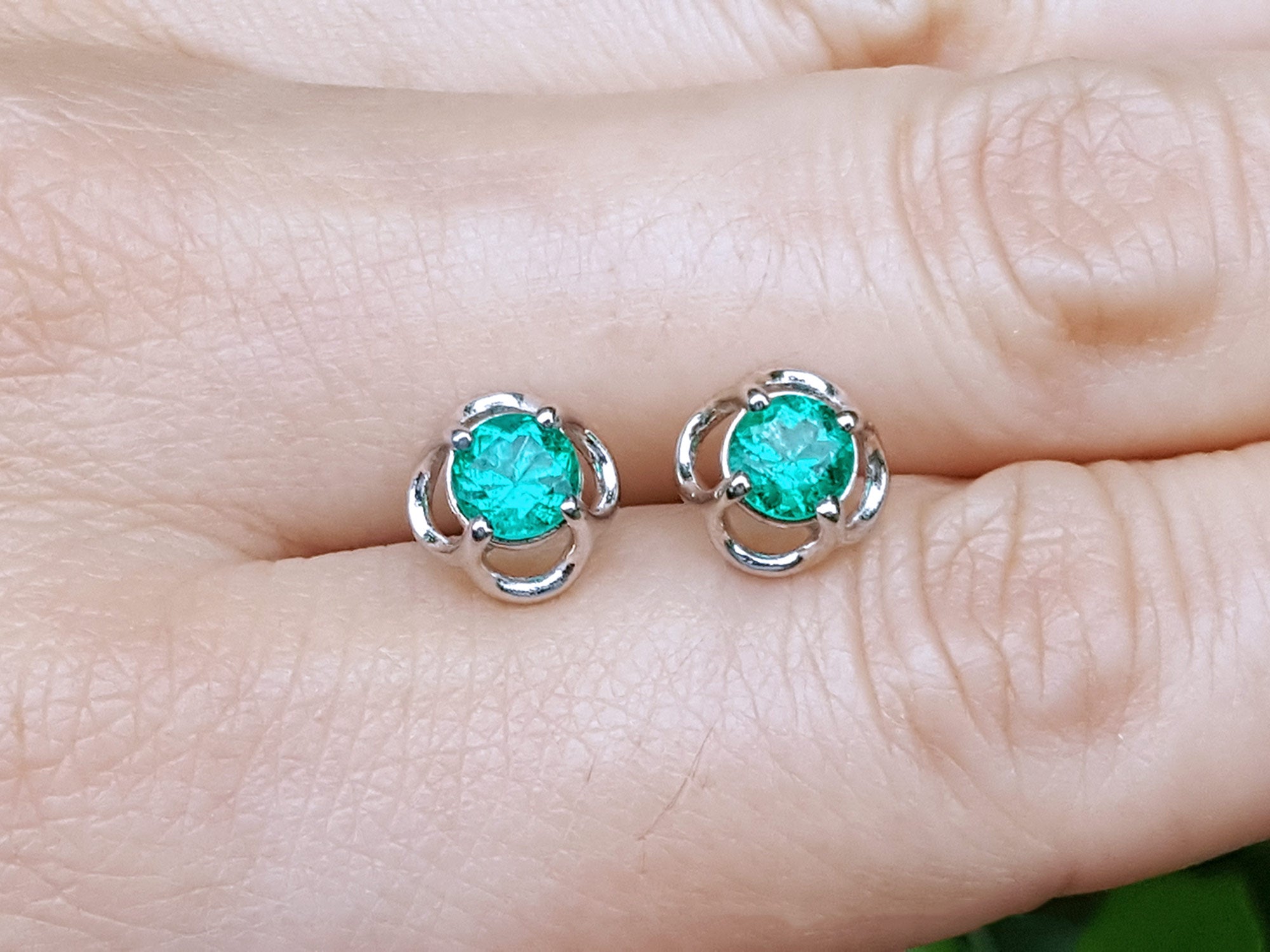Colombian emerald stud earrings held between fingers.