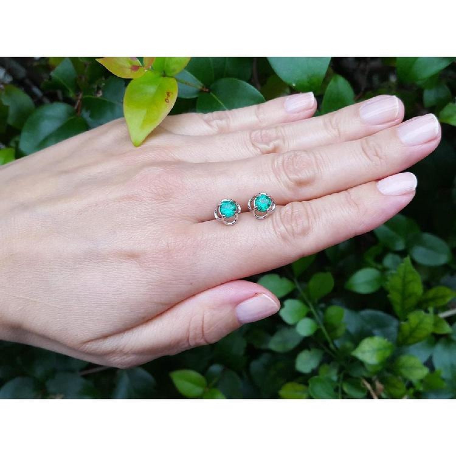 Tulip emerald stud earrings, 1.03 ct, 14K white gold, on a hand against green foliage.