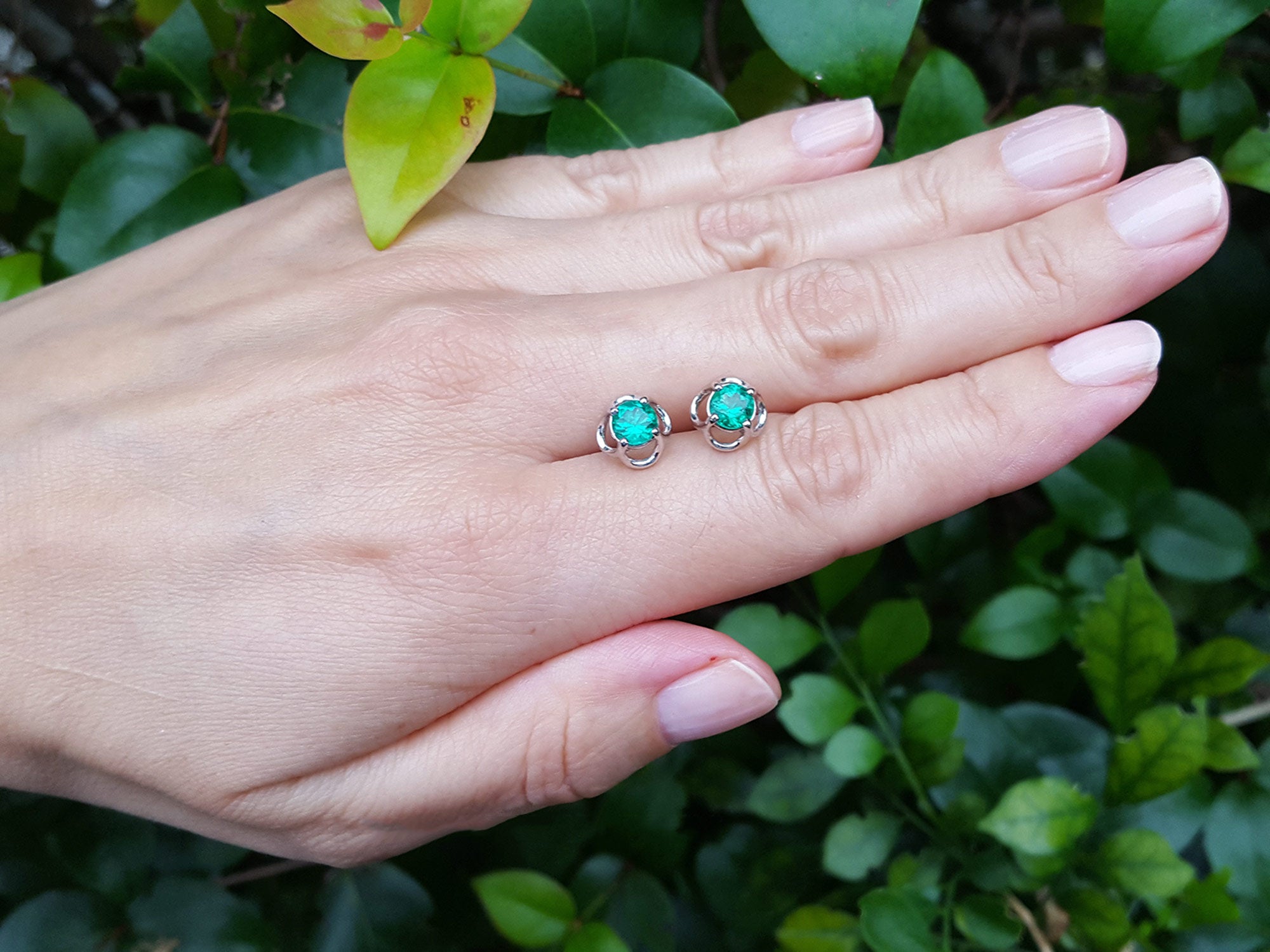 Hand wearing emerald tulip stud earrings with a green leafy background.