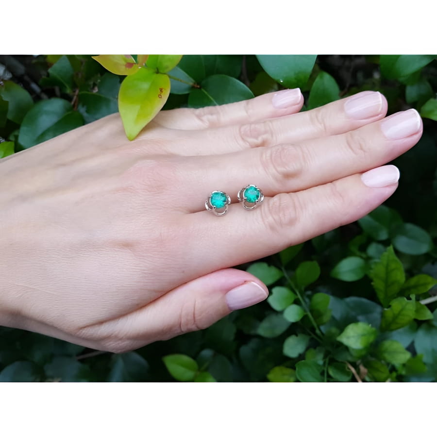 Tulip emerald stud earrings, 1.03 ct, 14K white gold, on a hand against green foliage.