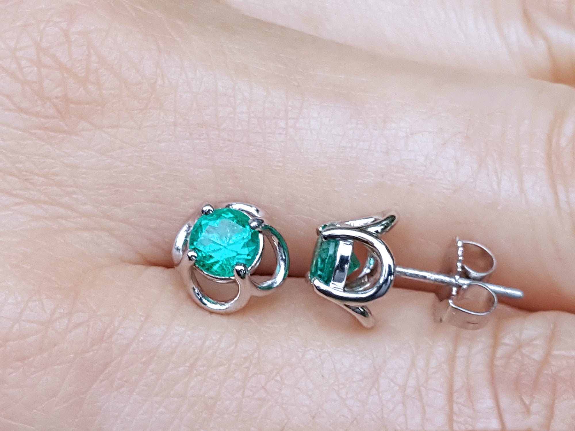 Colombian emerald tulip stud earrings on a person&#39;s finger.