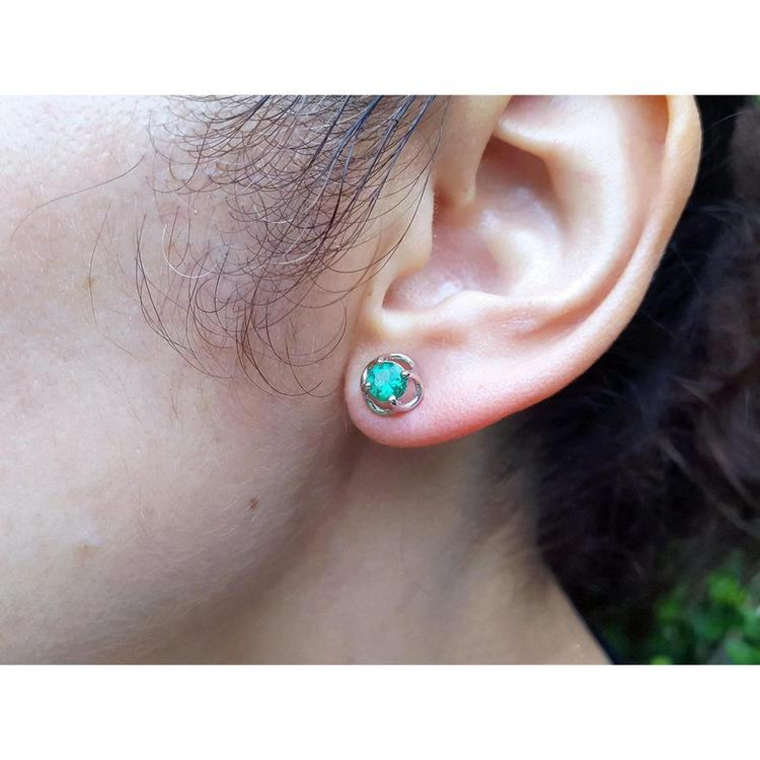Tulip emerald stud earrings with round green emeralds in 14K white gold, worn on an ear.