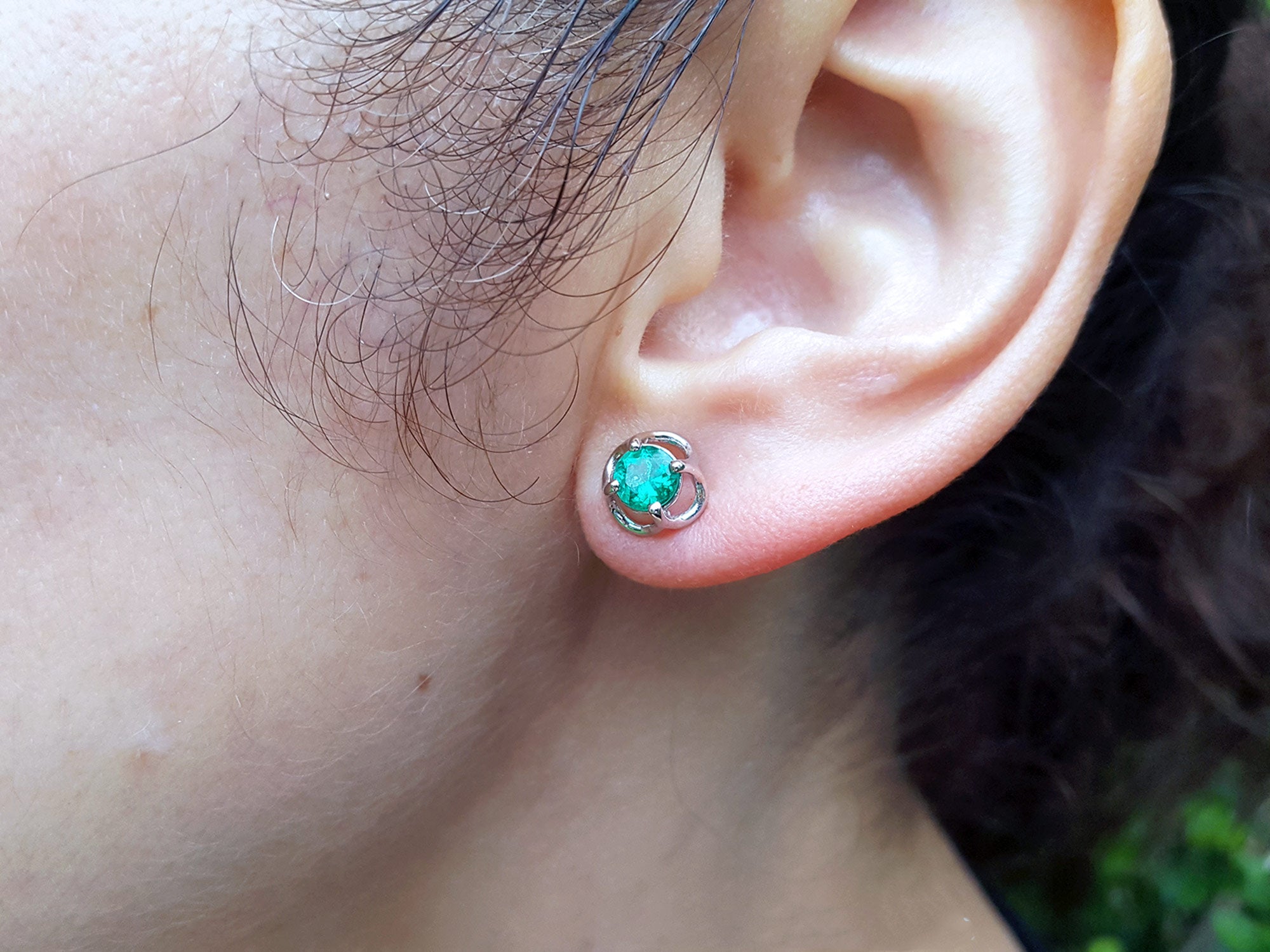Close-up of a woman&#39;s ear wearing a Colombian emerald stud earring with a blurred background.