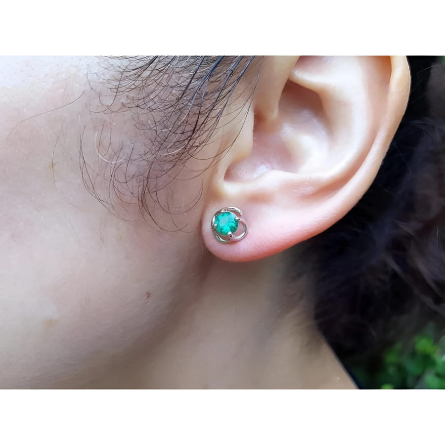 Tulip emerald stud earrings with round green emeralds in 14K white gold, worn on an ear.