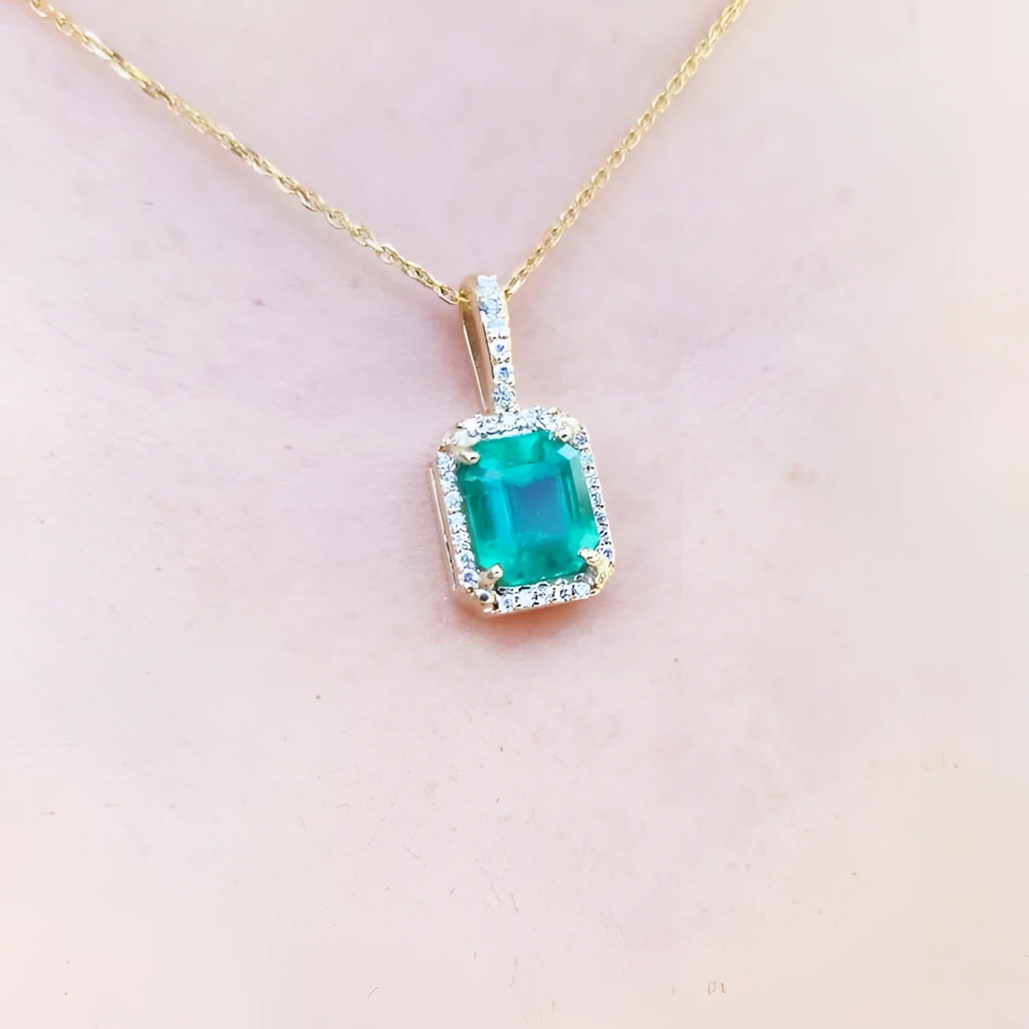 Emerald pendant on a gold chain against a light pink skin background