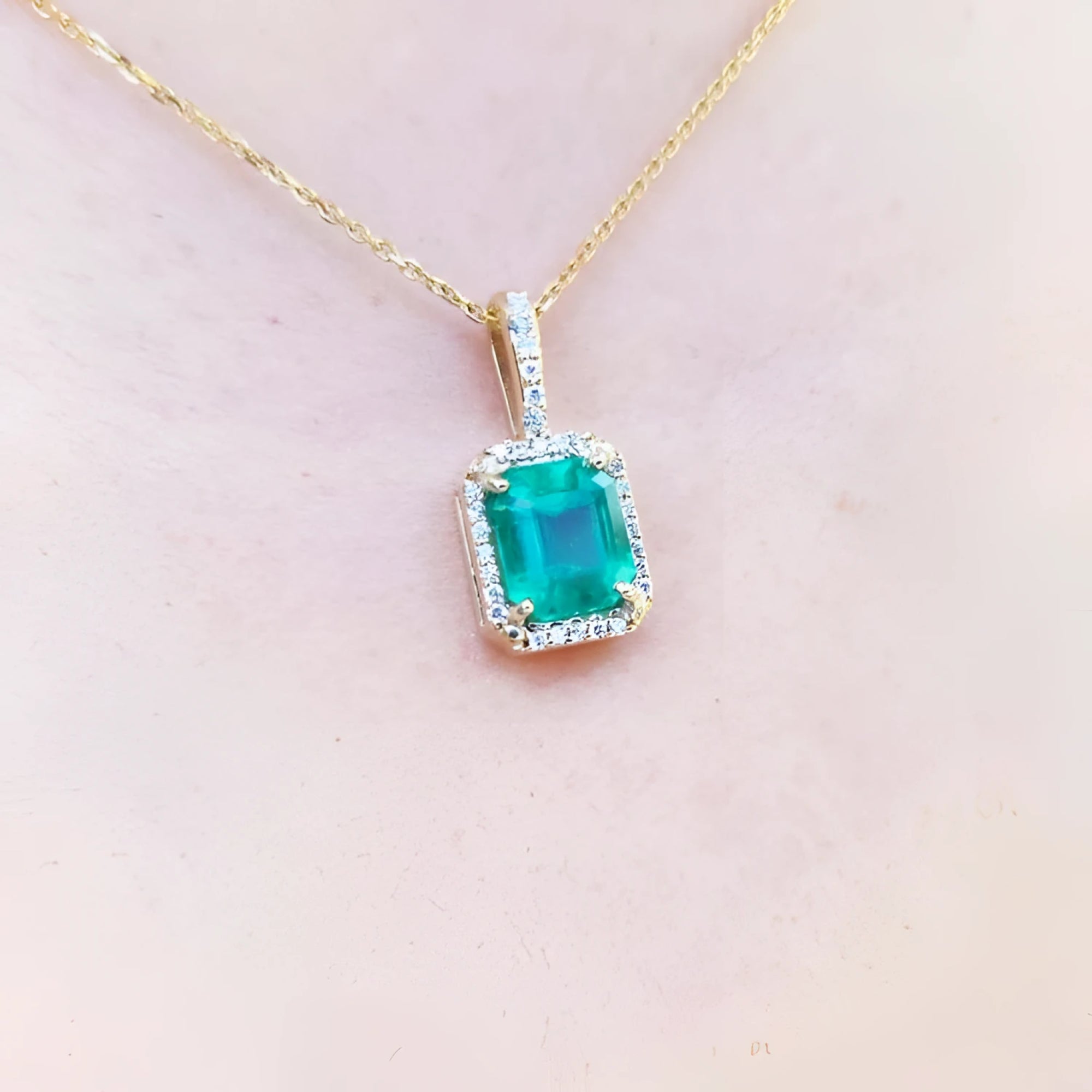 Emerald pendant on a gold chain against a light pink skin background