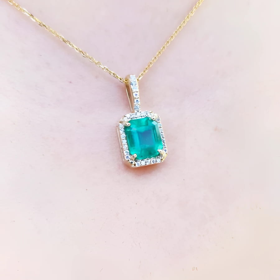 Emerald pendant on a gold chain against a light pink skin background