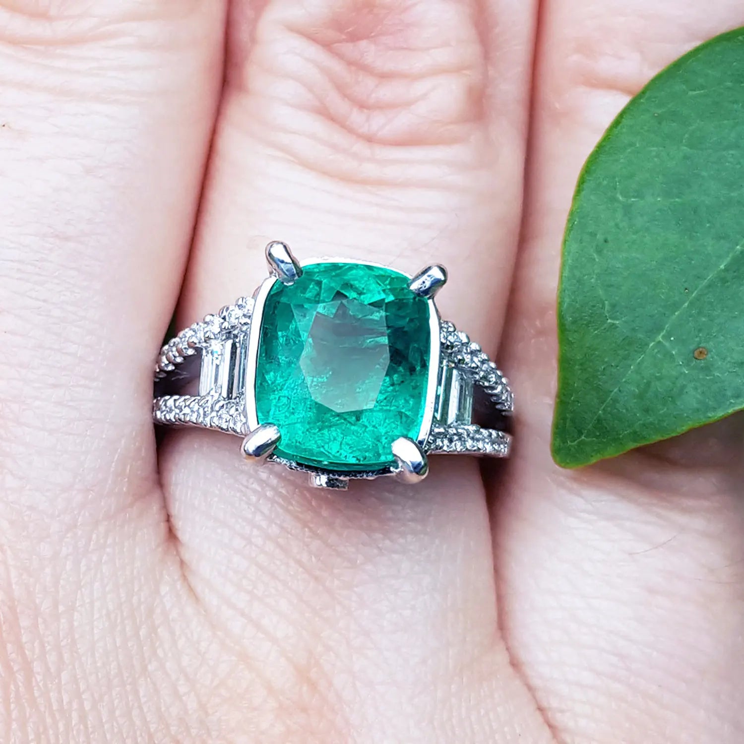 Anillo con esmeralda colombiana certificada posición frontal en dedo anular al lado de una hoja verde.
